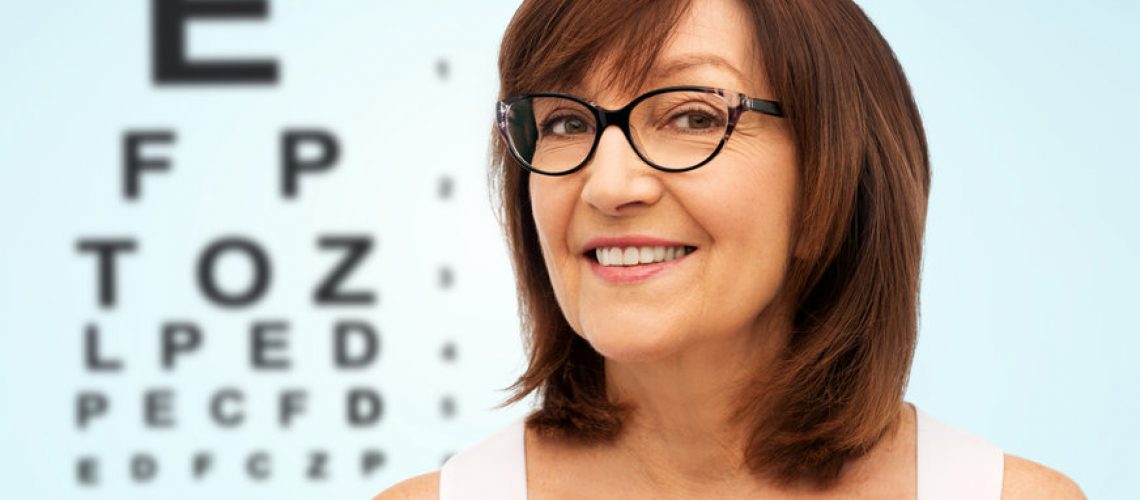 beauty, vision and old people concept - portrait of smiling senior woman in glasses over eye test chart on blue background